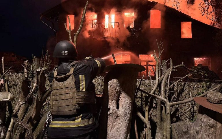A firefighter by a burning house in Kyiv after a drone attack